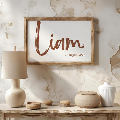 Personalized baby name sign with the name Liam and birth date in a brown brush font, framed and displayed on a rustic table with natural decor elements.