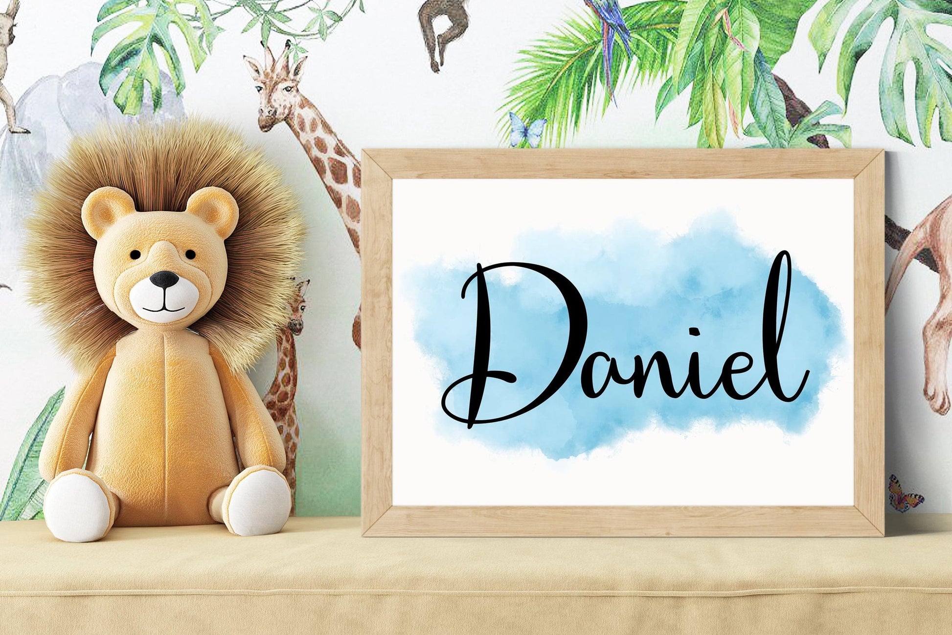 Custom nursery name sign reading Daniel on blue watercolor background, styled beside lion plush toy with jungle-themed wallpaper, perfect for custom nursery decor.