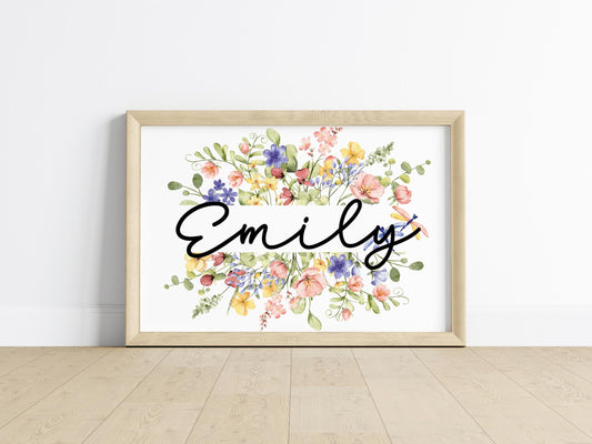 Hands holding a framed wildflower name sign with customizable text and intricate floral patterns, highlighting its charm as a personalized baby gift.