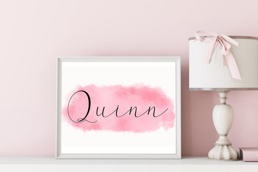 Framed custom name print of Quinn on pink watercolor background, styled on a nursery shelf with lamp decor, ideal baby name sign and nursery decor.