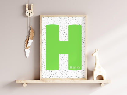 Personalized initial nursery sign with large green letter H and dotted background on a wooden shelf with decor