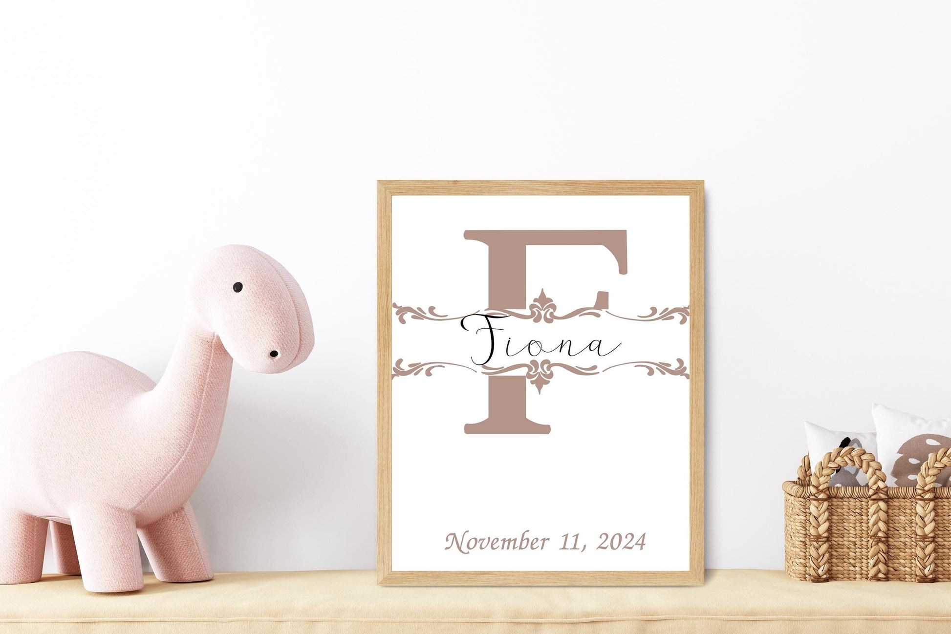 Custom baby name sign with a light taupe initial styled alongside a pink dinosaur plush, great for nursery wall decor or baby shower gifts.