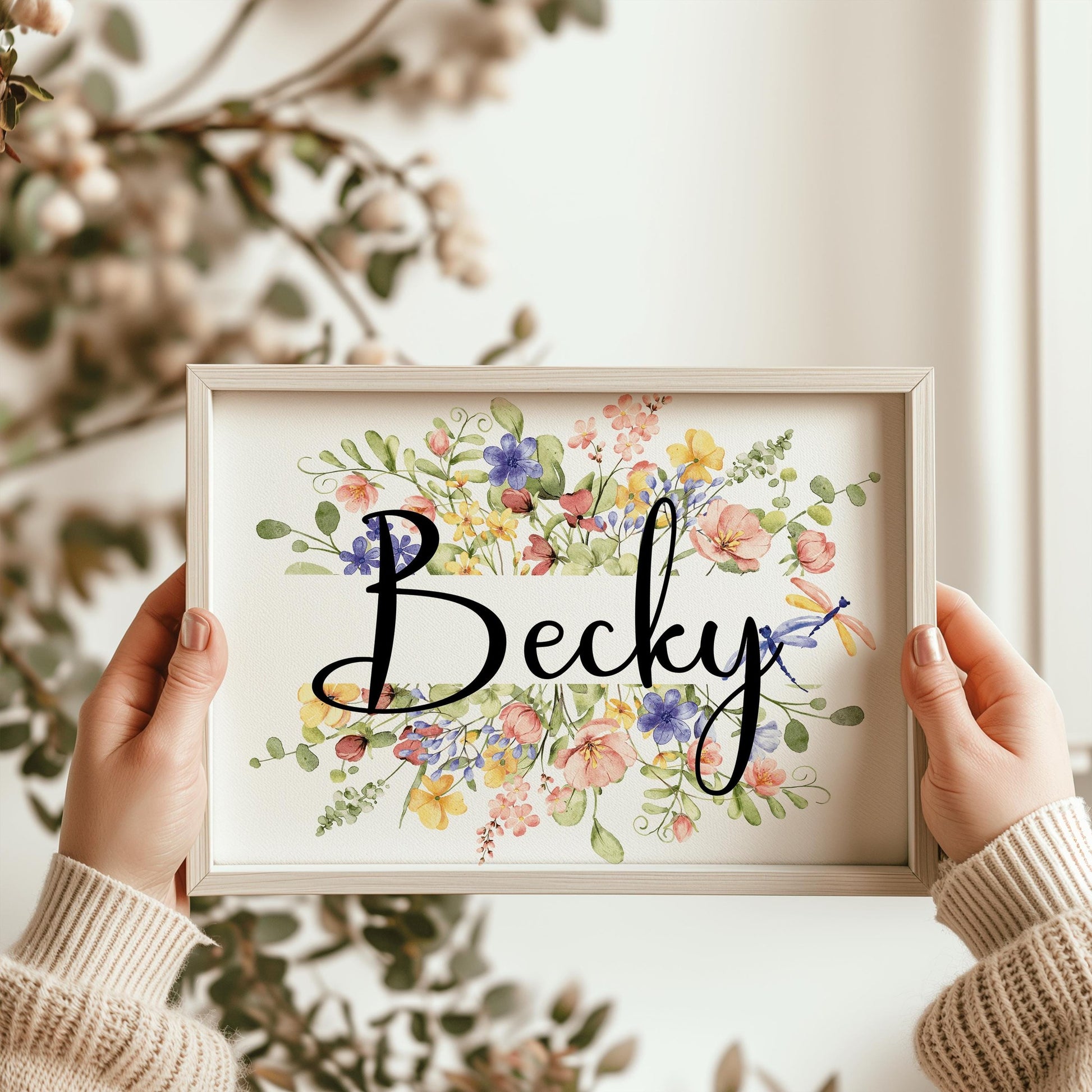 A framed floral name sign featuring delicate wildflowers, perfect for custom nursery decorations and unique baby shower gifts.