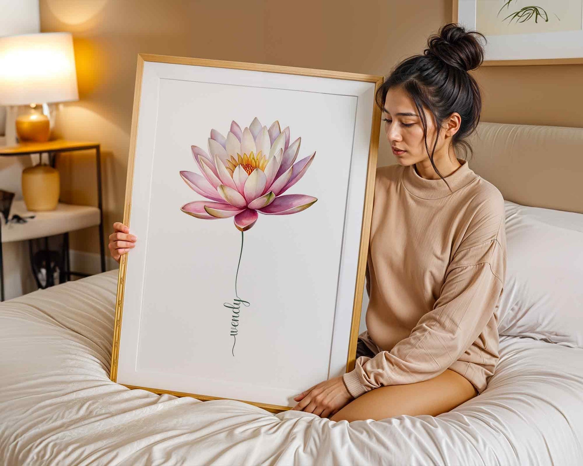 A person sitting on a bed holding a framed pink lotus flower name sign, ideal for personalized gifts or decor.